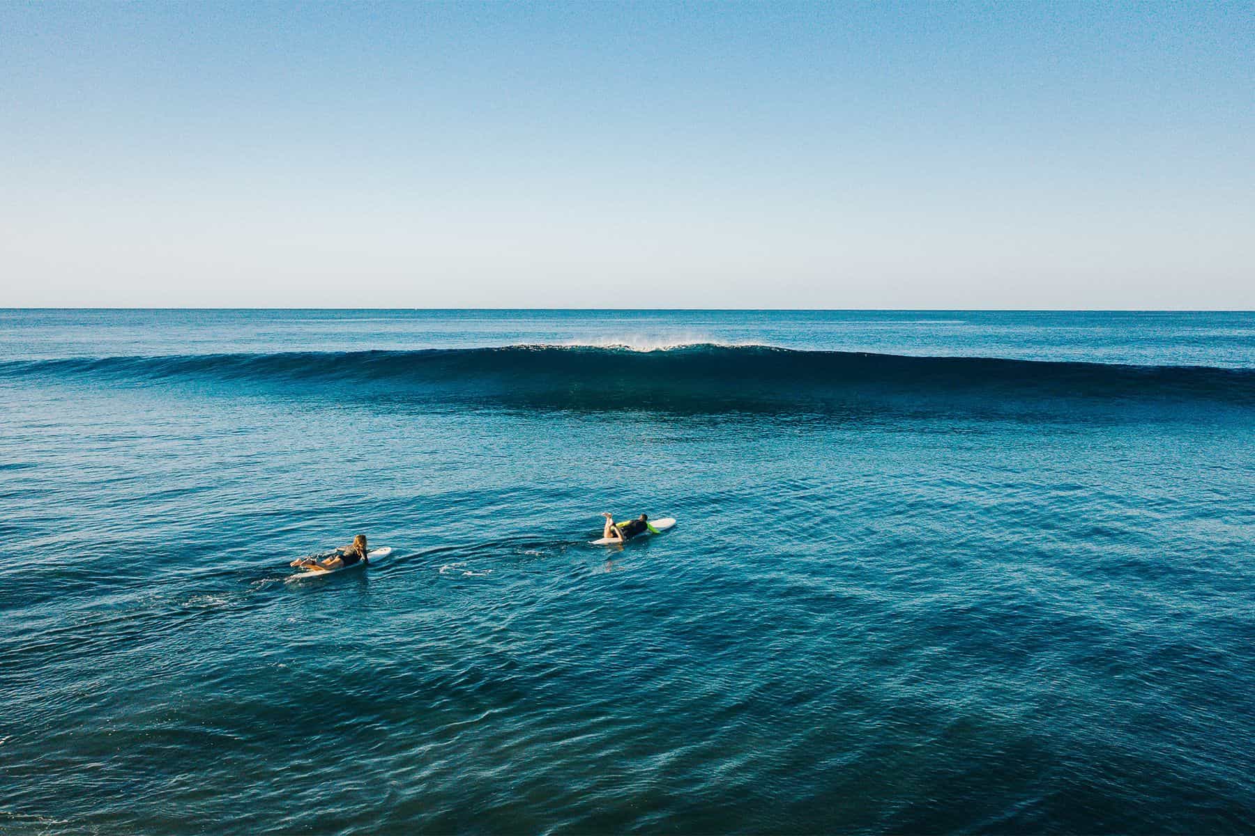 two surfers paddlingout to an empty peak at surf simply in costa rica