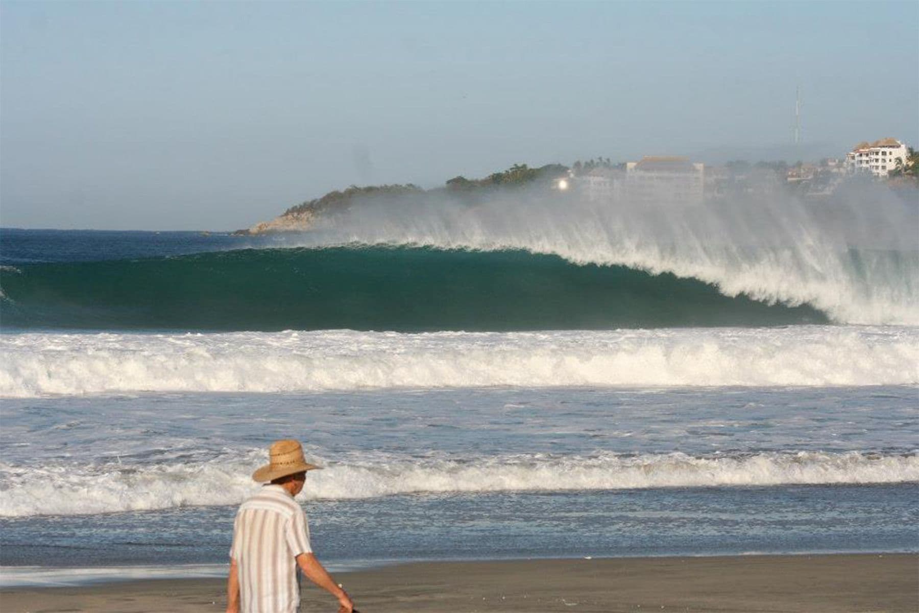 man walking on the beach in front of a breaking wave at puerto escondido, mexico