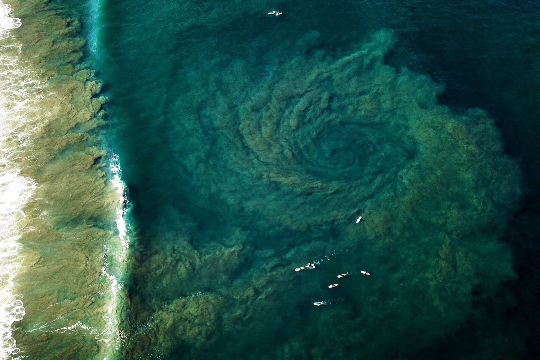 aerial drone photograph of surfers and a rip plume at playa guiones in costa rica