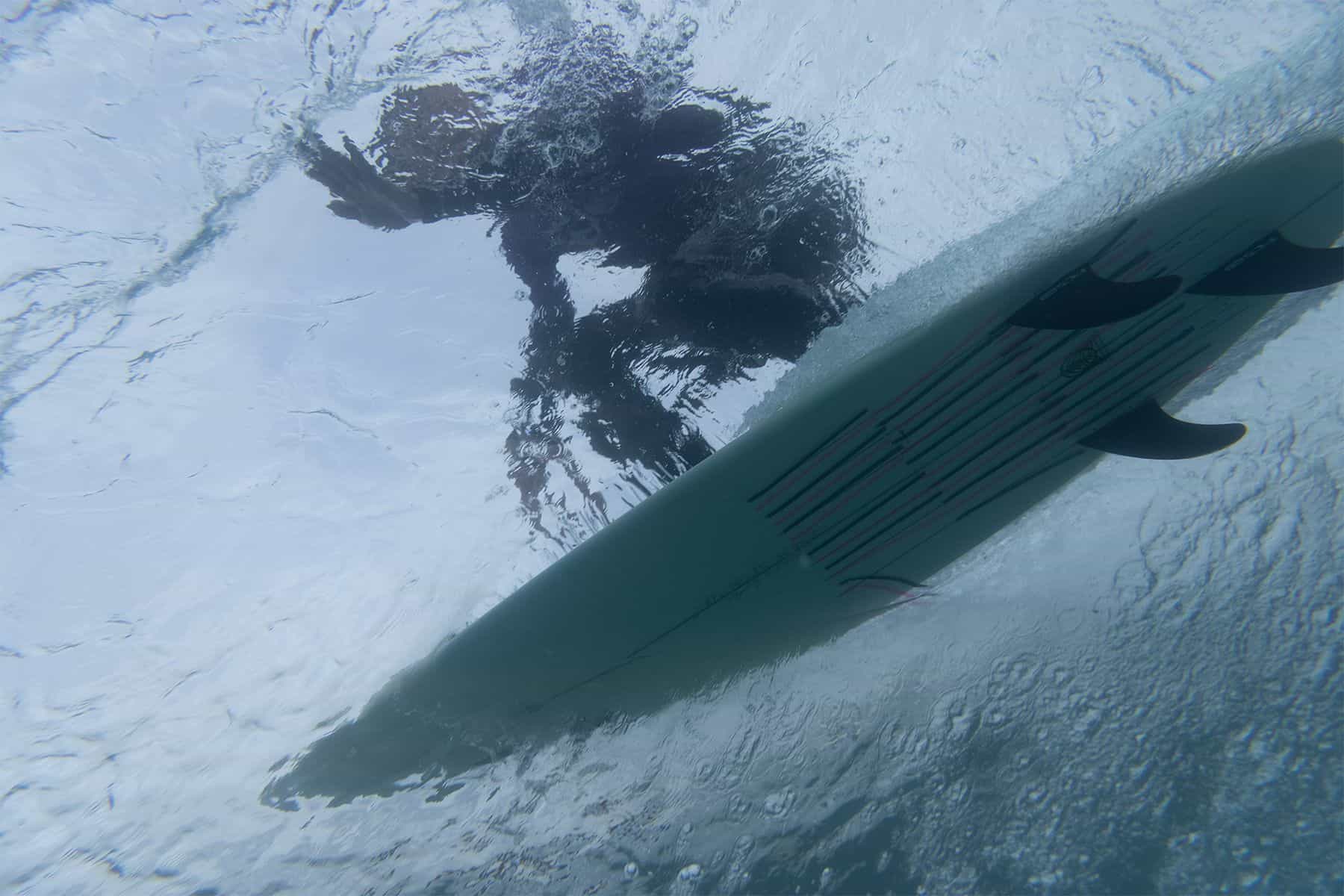 underwater view of a surfer going along a wave with tell tale ribbons on the bottom of his surfboard